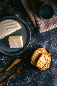 Top view of fresh cheese and crunchy bread placed on dirty black table near napkin and dishware in kitchen