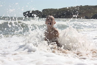 Boy splashing water while playing in sea during summer