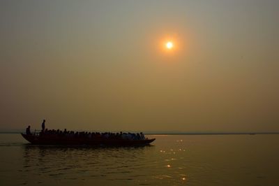 People in boat sailing on river against clear sky during sunset