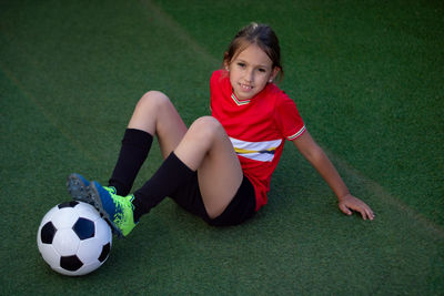 Portrait of smiling girl with soccer ball sitting on field