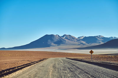 Scenic view of road and mountains against clear blue sky
