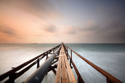 Pier over sea against sky at sunset