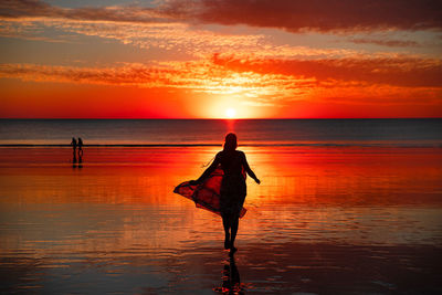 Silhouette woman standing on beach against sky during sunset