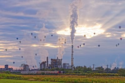 Silhouette hot air balloons flying over factory during sunset