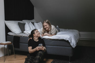 Homosexual female couple sitting on bed and looking at cell phone