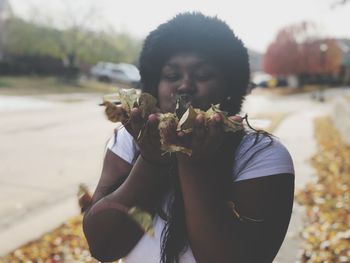 Girl blowing leaves in city during autumn