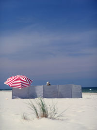 Woman behind striped canvas with red umbrella at beach against sky