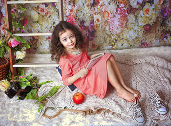 High angle portrait of girl with book sitting against wallpaper