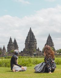 People sitting outside temple on building against sky