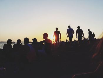 Silhouette people at beach against sky during sunset