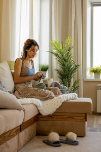 Woman crocheting while sitting on couch at home