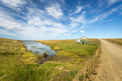 Dirt road amidst field against sky