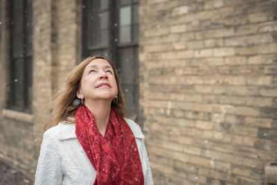 Woman standing by brick wall during snowfall