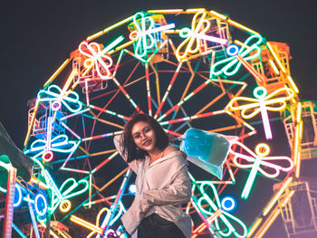 Portrait of woman with illuminated ferris wheel in amusement park