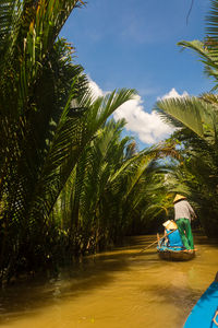 Rear view of people on boat at river by trees