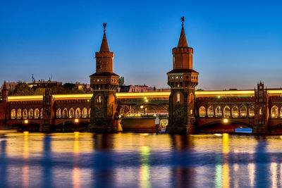 Illuminated bridge over river against blue sky in city