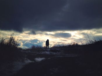 Man standing on field against cloudy sky