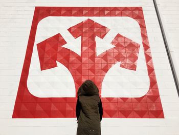 Rear view of person standing against wall with red directions