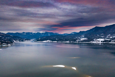 Aerial view of lake by mountains against sky during sunset