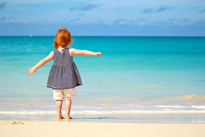 Rear view of girl standing on beach against sea