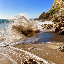 Sea waves splashing on rocks against clear sky