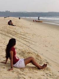 Woman sitting on beach by sea against sky