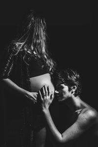 Man touching pregnant woman belly against black background