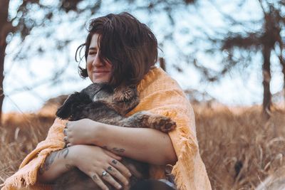 Smiling young woman embracing dog on field