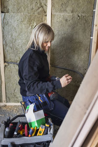 Smiling blond female technician with drill machine by tool box