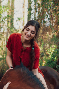 Smiling young woman sitting on horse in forest