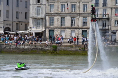 Man flyboarding in sea against building in city