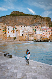 Woman walking on building by sea against sky in city