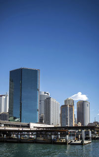 Modern buildings by sea against clear blue sky