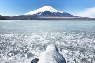 Low section of snowcapped mountain by lake against sky