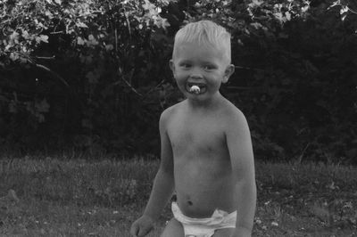 Portrait of shirtless boy sucking pacifier on field