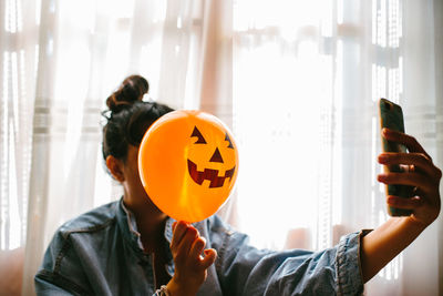 Close-up of woman holding halloween decoration against face and taking selfie at home