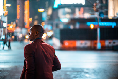 Rear view of man looking at illuminated city street