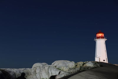 Lighthouse by rocks against sky at night