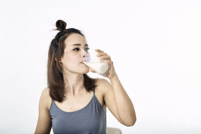 Portrait of young woman drinking drink against white background