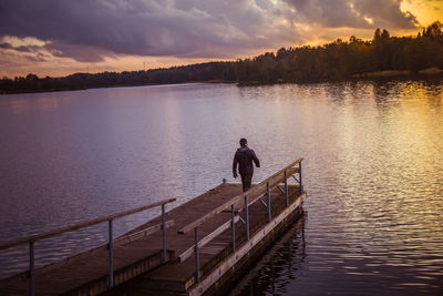 Men on pier over lake against sky during sunset