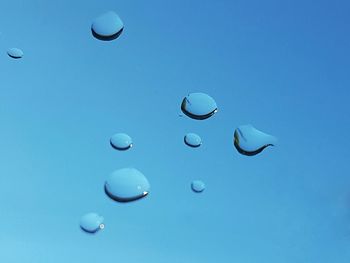 Close-up of water droplets on window against blue sky background