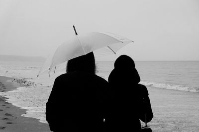Rear view of silhouette couple at shore against sea