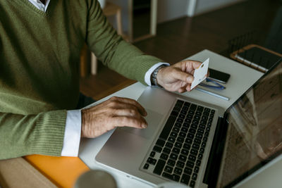 Midsection of mature man working on laptop while sitting at home