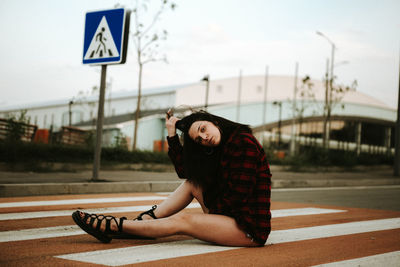 Young woman sitting on road against sky