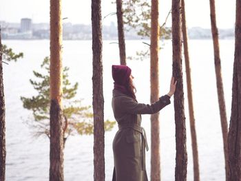 Woman standing by tree trunk by sea against sky