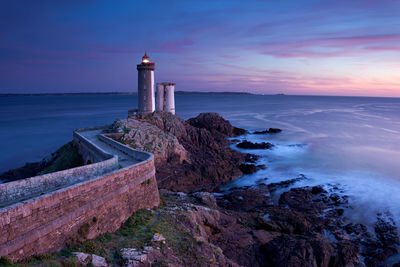 Lighthouse by sea against sky during sunset