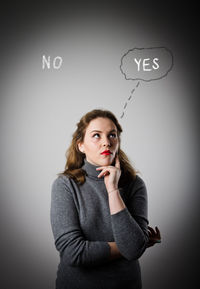 Portrait of a young woman standing against gray background