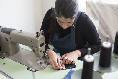 High angle view of mature female tailor measuring fabric on sewing machine at laundromat