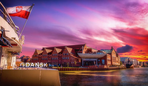 Illuminated buildings by river against sky during sunset