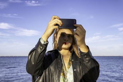 Woman taking selfie standing by sea against sky